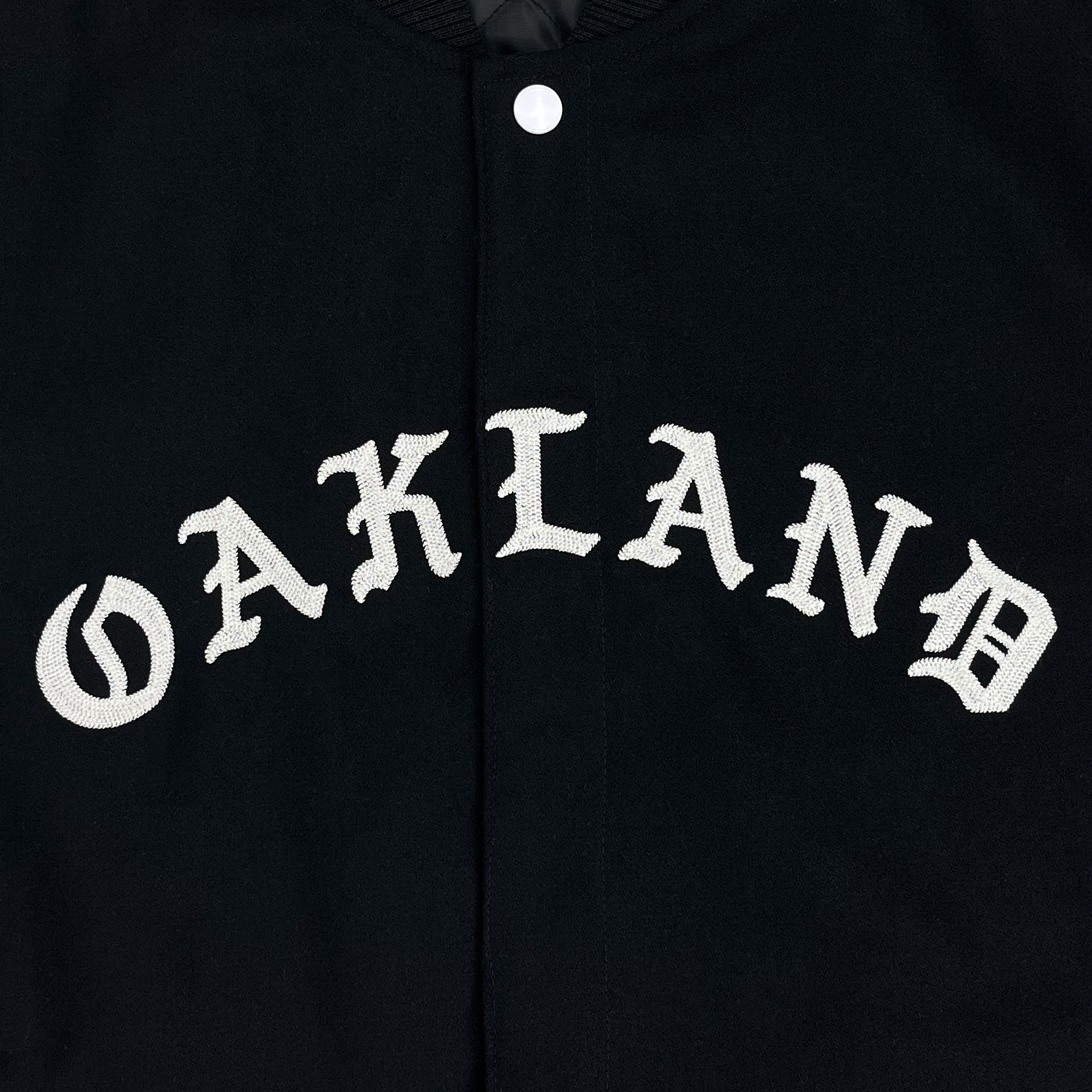 Large embroidered OAKLAND wordmark on the front chest of a black and white varsity jacket.