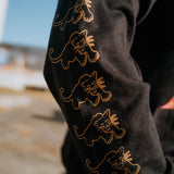 Close-up angle on female model of gold Black Panther outlines on repeat on the sleeve of a black long-sleeve t-shirt sleeve.