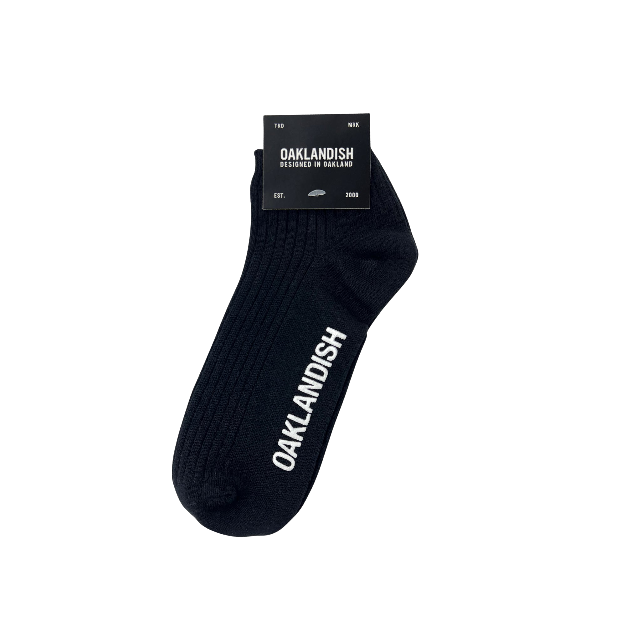 A single black "Grip Low Crew Sock" by Oaklandish features the word "OAKLANDISH" printed in white along its side. This classic example of Oaklandish crew socks comes attached to black packaging that reads "OAKLANDISH," "Designed in Oakland," "EST. 2000," and size information labeled as "TBD MK." The sock is displayed against a plain white background.