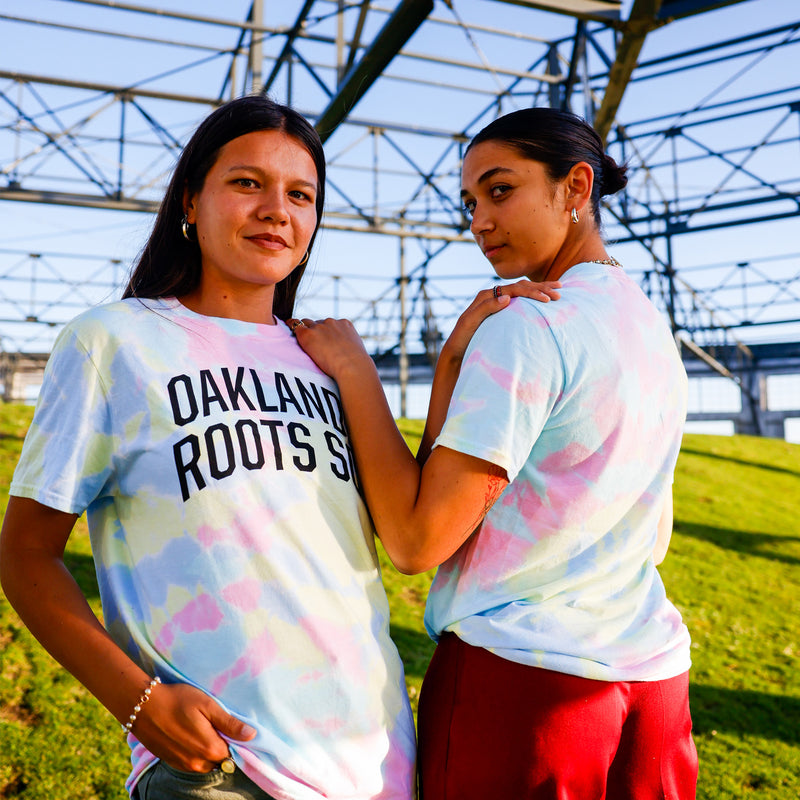 Models wearing Oakland Roots SC Peace, Love, and Oakland tie dye pastel tee outdoors. 