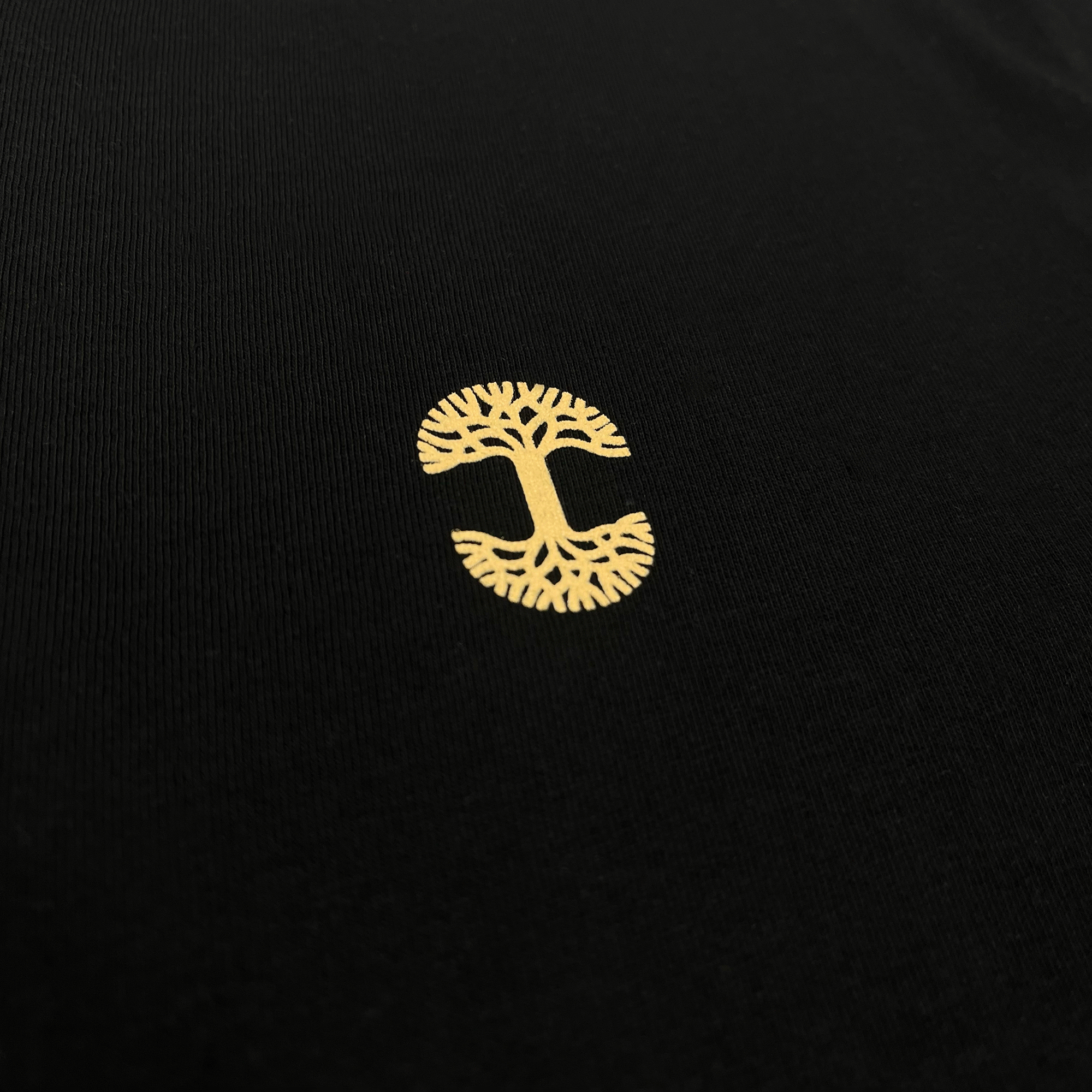 Close up yellow Oaklandish tree log on chest of black t-shirt.