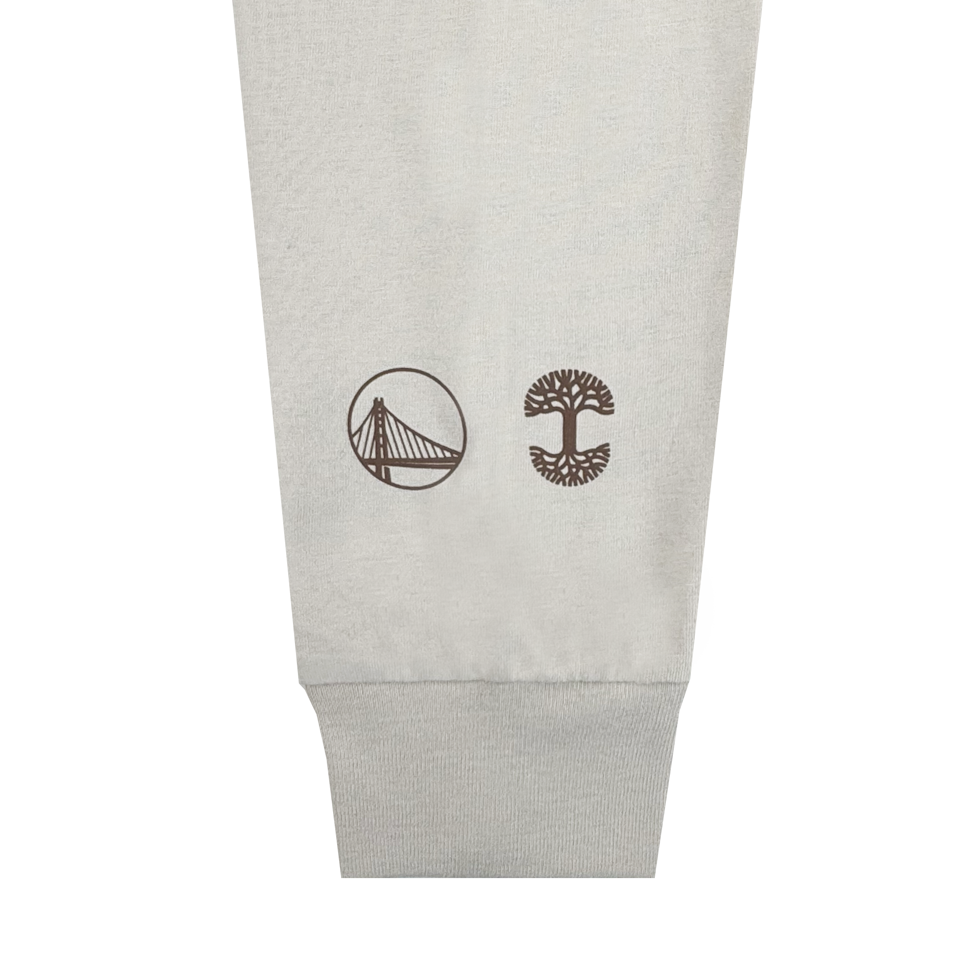 A close-up of the Pirate Black-Letter LS Tee by GSW shows a light beige cuff with two small brown logos—a cable-stayed bridge in a circle on the left and a stylized tree on the right—against a plain white background.