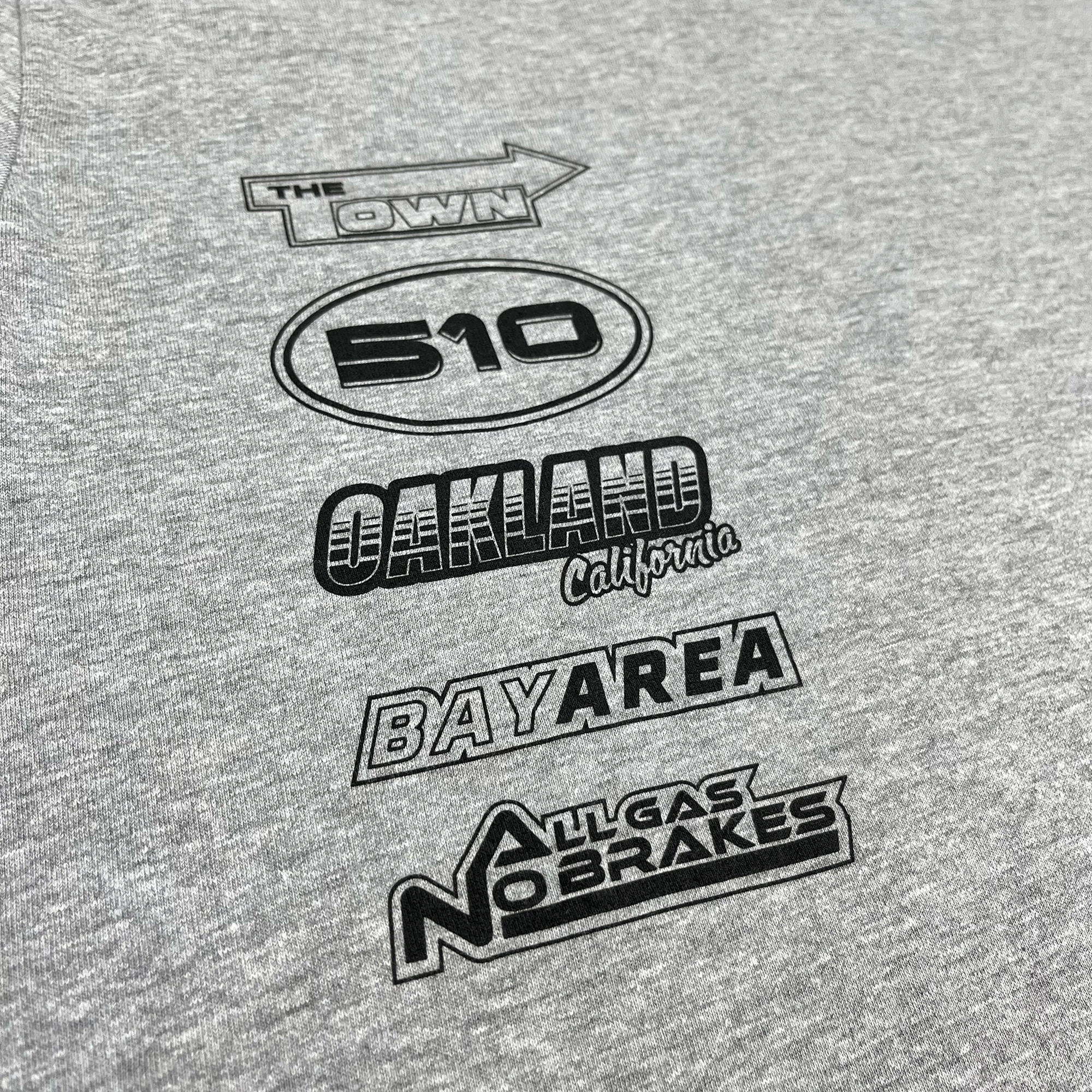 Close-up of black race car-inspired design and Oaklandish tree logo on a grey long-sleeved t-shirt.