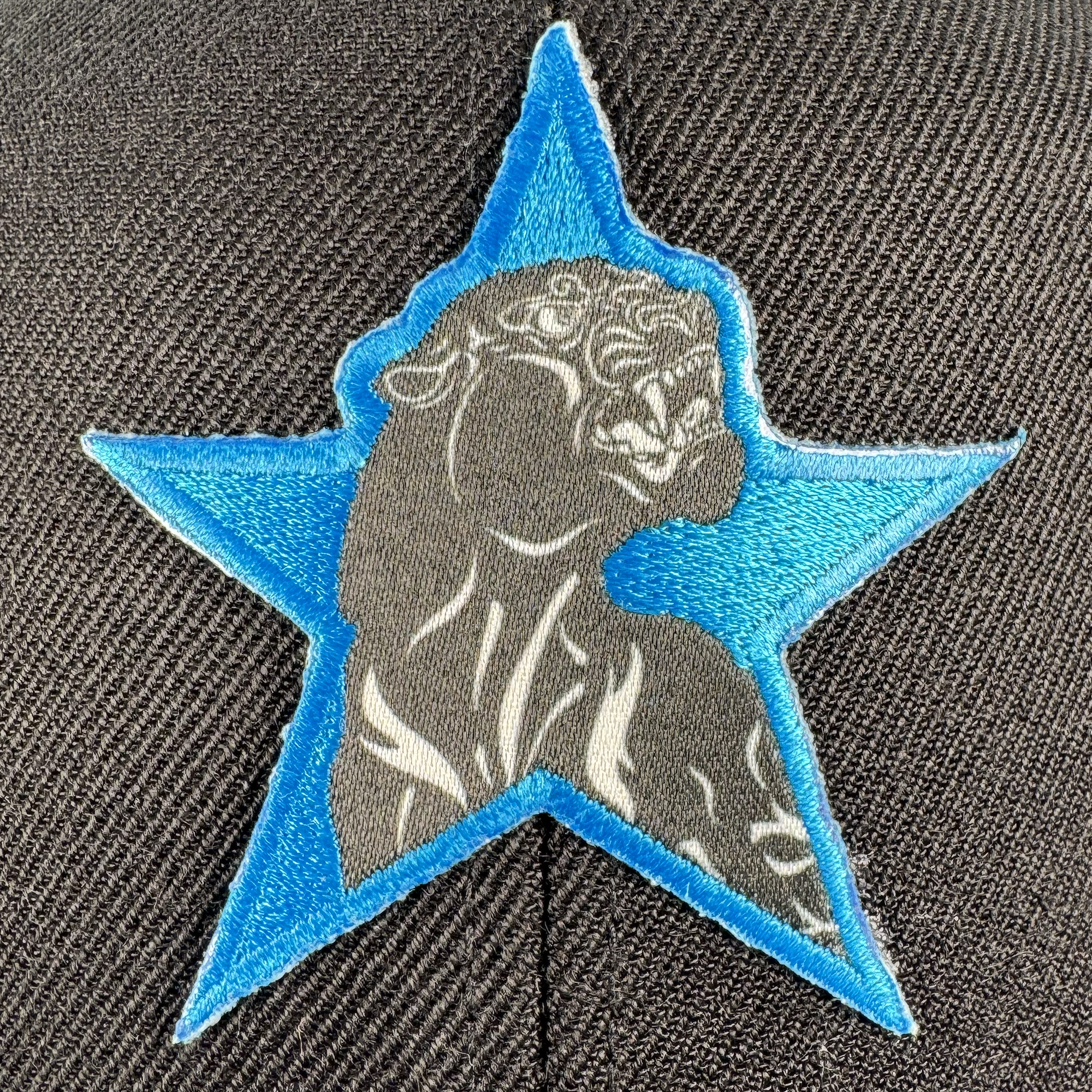 The Oaklandish Power of the People Dad Hat features a close-up of its textured black fabric, embroidered with a blue star and a stylized classical bust, evoking the spirit of Black Panther Party apparel.