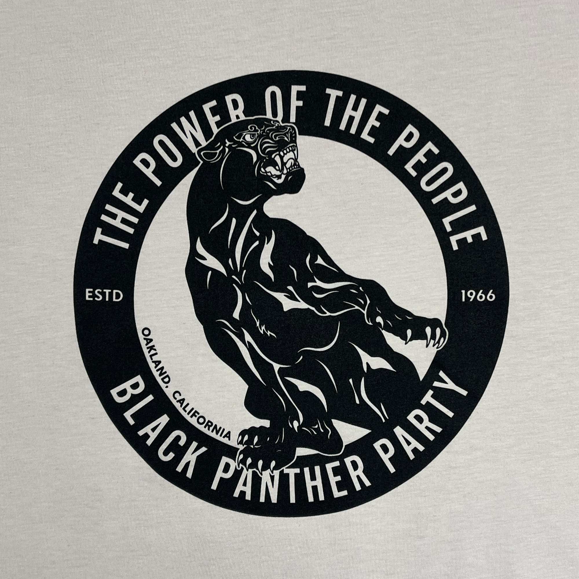 A black panther emblem in a mid-roar position graces the dark circular border of the "Power of the People Tee" by Oaklandish. The border is encircled with text reading "The Power of the People" at the top and "Black Panther Party" at the bottom. Within the circle, "ESTD 1966" and "Oakland California" are also inscribed, capturing Stealworks' essence.