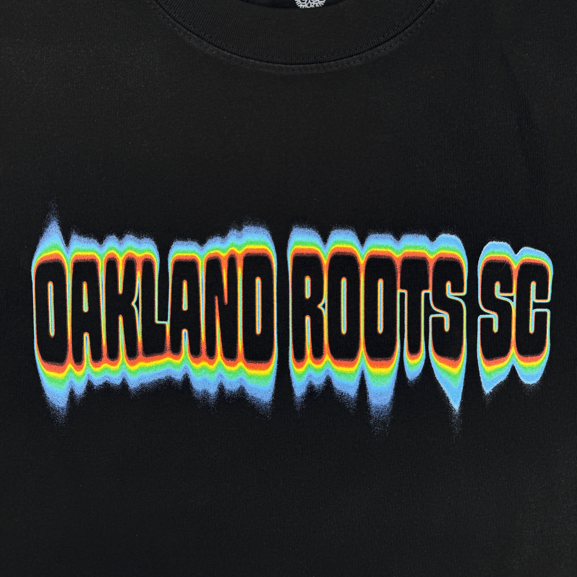 The Oakland Roots SC Acid Tee features bold, distorted "OAKLAND ROOTS SC" text with blue, orange, yellow, and white outlines for a vibrant wavy effect on black—perfect for showing your Roots SC pride.