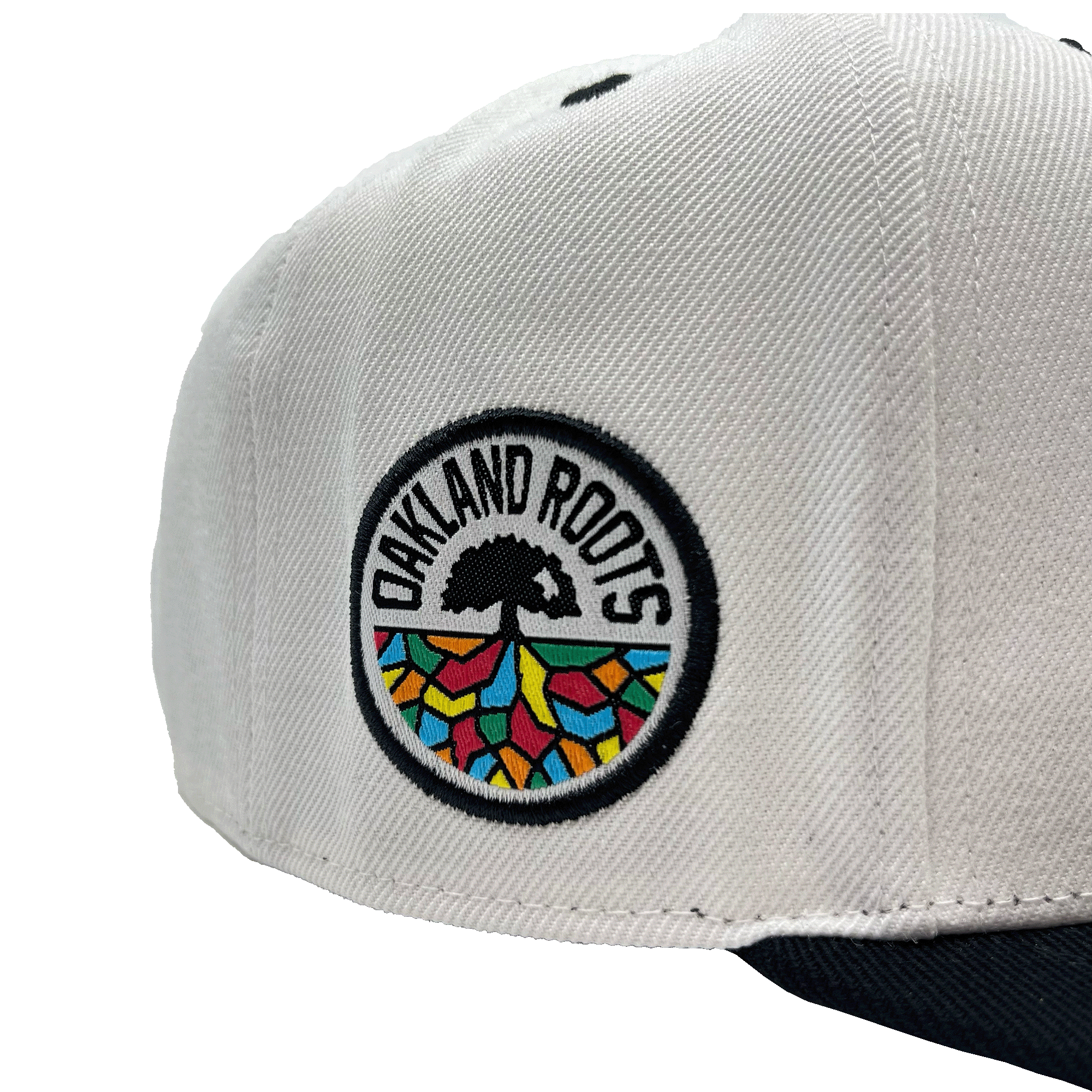Close-up of full color circle Oakland Roots circle logo patch on the side of white snapback hat.