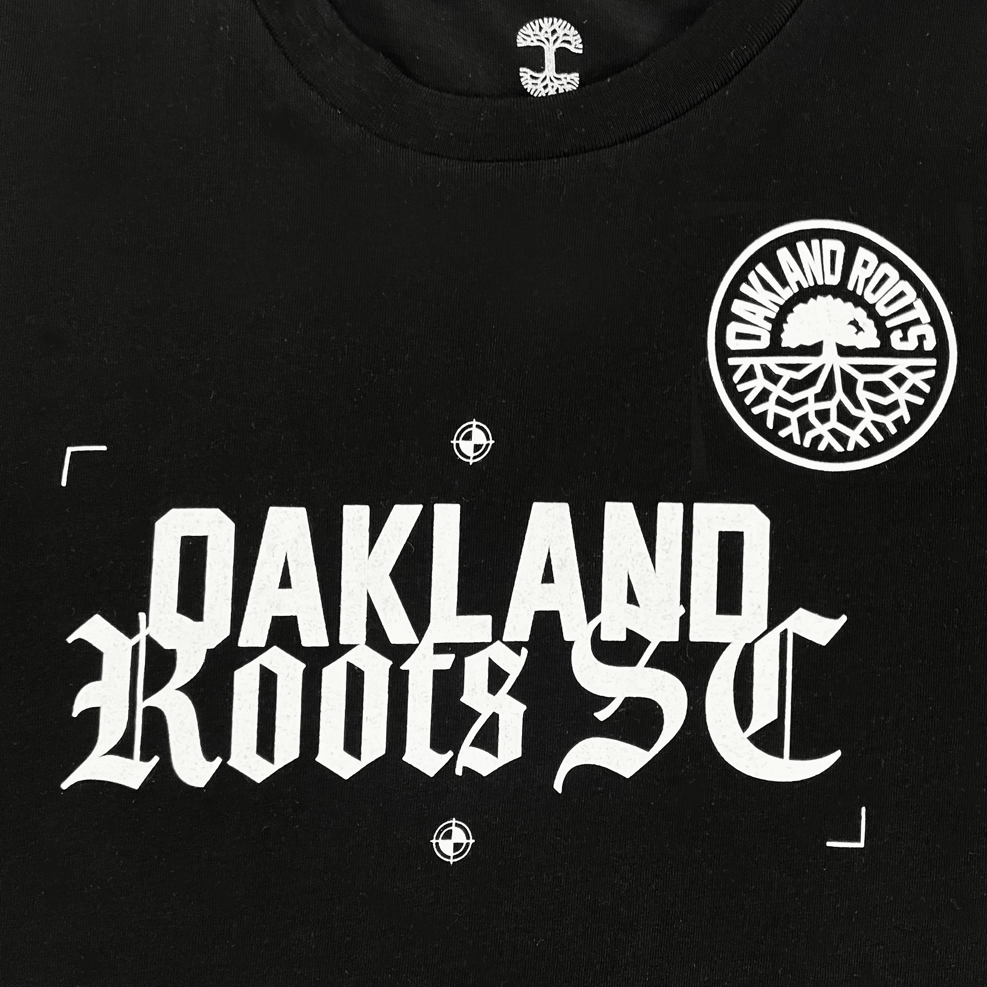 Close-up of white OAKLAND ROOTS SC wordmark in old-time font and circle logo on the chest of a black t-shirt.