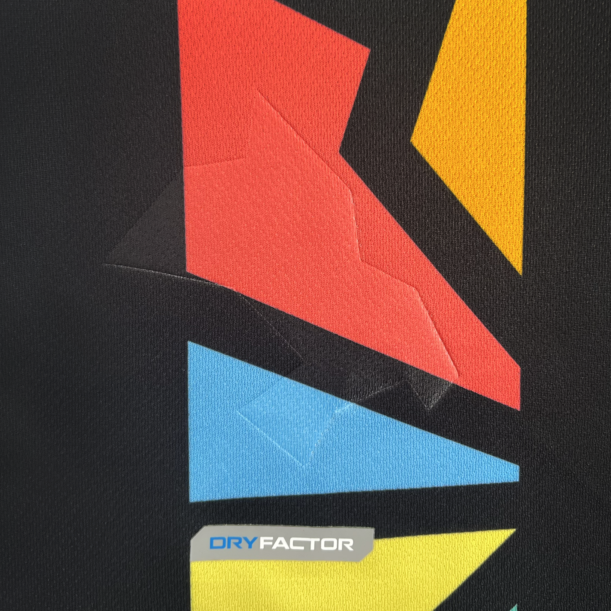 The Custom Unisex Oakland Roots SC 2025 First Kit features an abstract design on black fabric with large angular shapes in red, yellow, and blue. It includes a shiny embossed texture and displays "DRY FACTOR" in blue and black at the bottom.