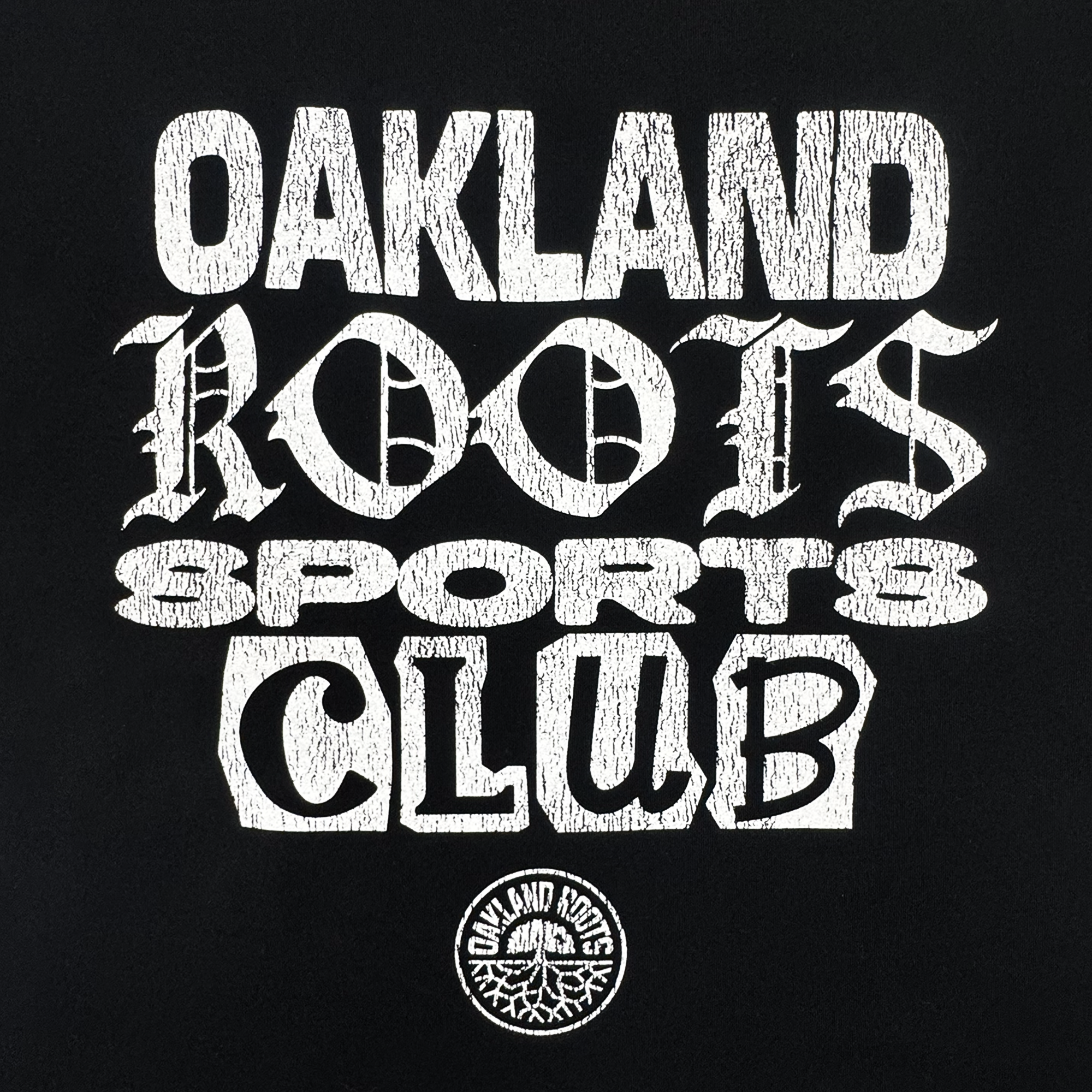 The Oakland Roots SC Multi Text LS Tee is a vintage-style black long sleeve shirt with an oversized fit, "Oakland Roots Sports Club" in mixed distressed fonts, and a small circular crest with tree root design at the bottom center.