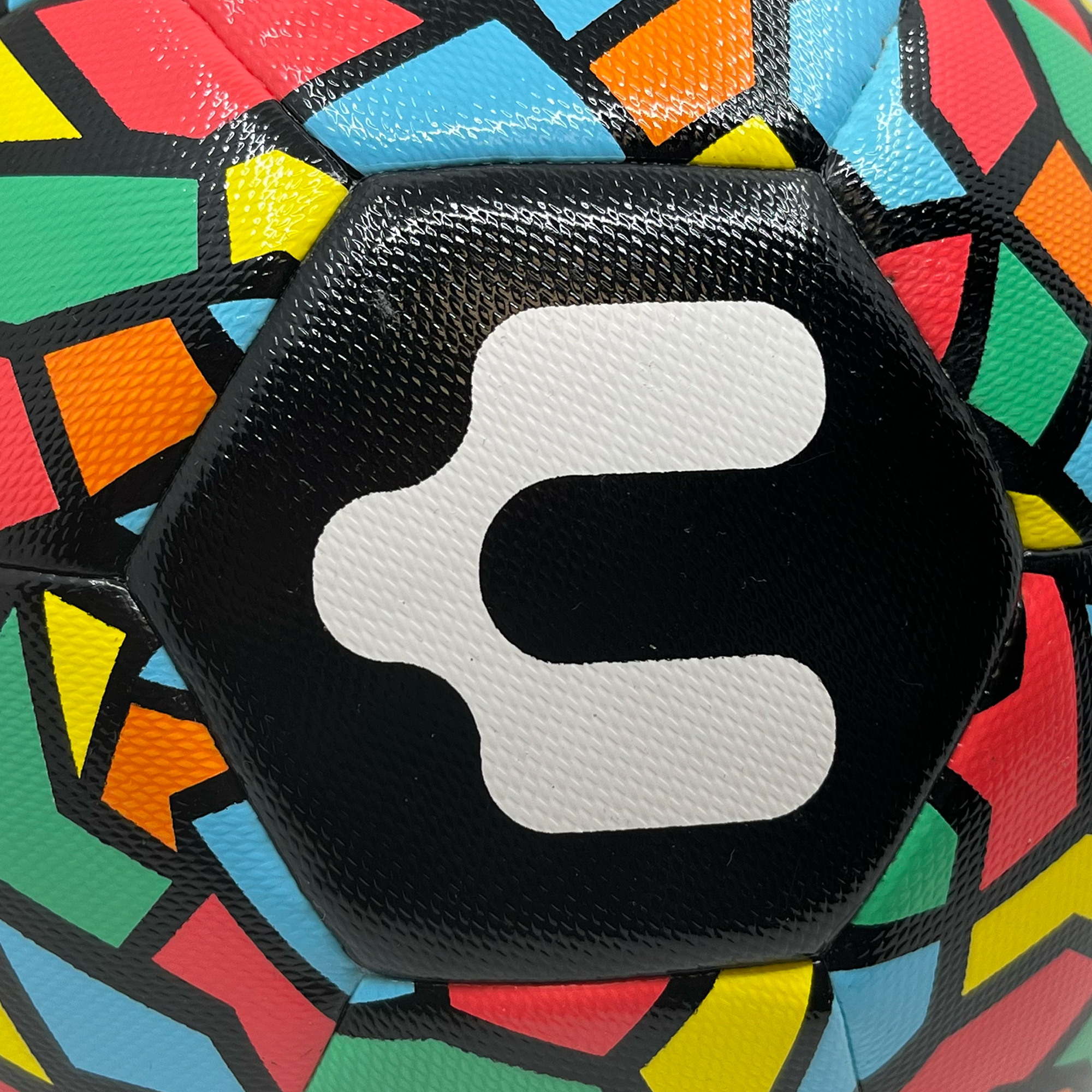 A close-up image of the Oakland Roots SC x Charly Size 5 Soccer Ball. The ball showcases a geometric pattern composed of hexagonal segments, each filled with vibrant colors like green, red, yellow, orange, and blue. A central black hexagon prominently features a bold white abstract "Charly x Oakland Roots SC" logo.