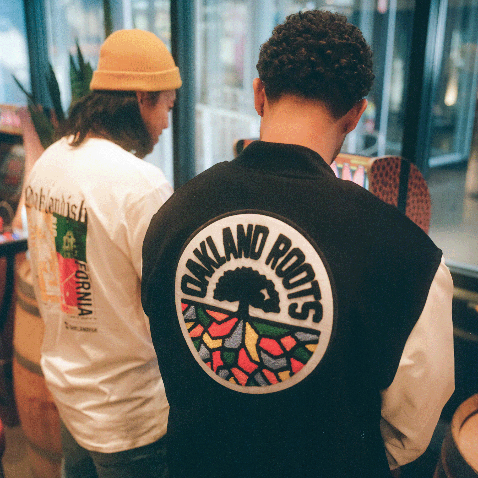 Two men, backs to camera, standing in a shop wearing Oaklandish lifestyle apparel. 