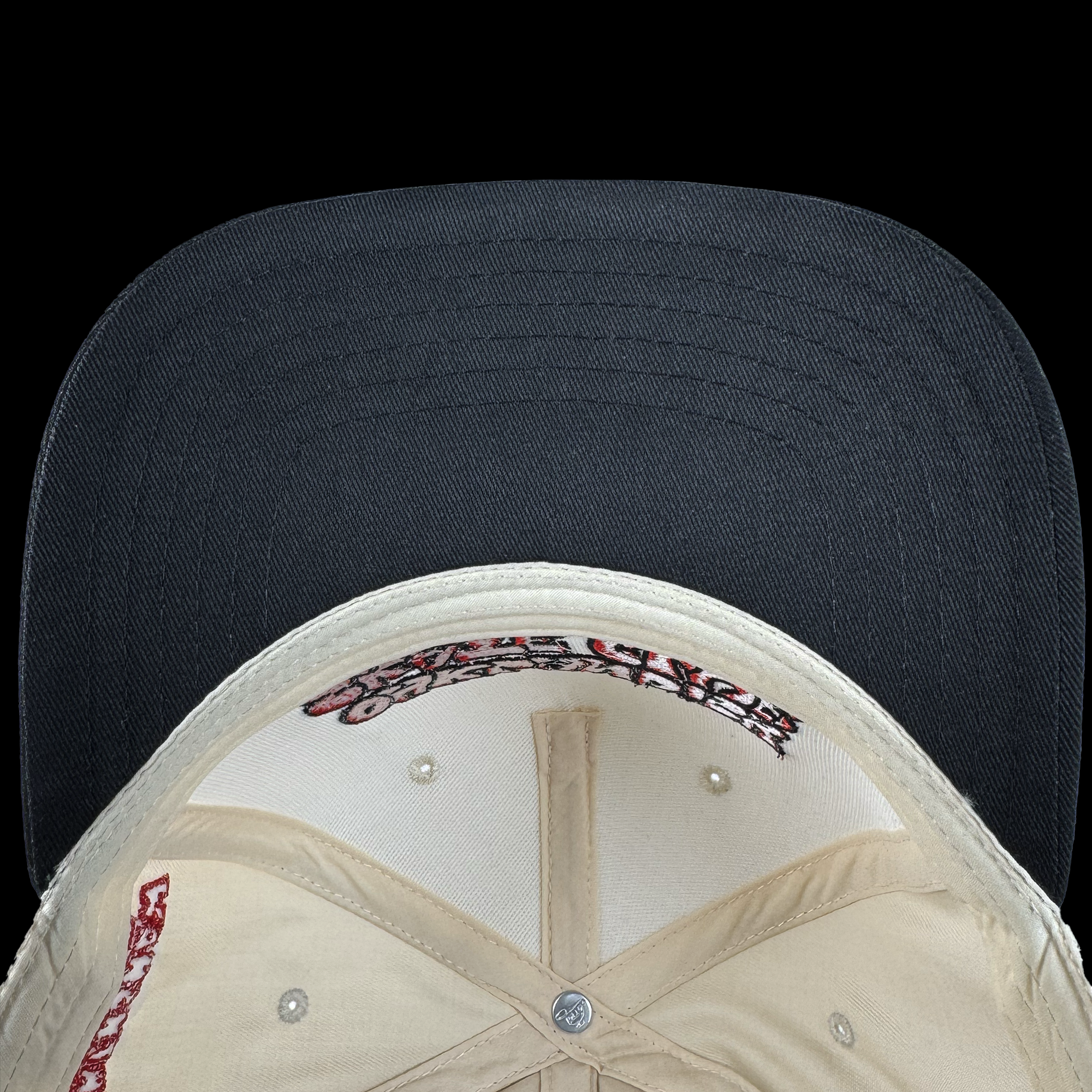 Top-down view of the Oaklandish Skate Club 2-Tone Hat by Oaklandish, featuring a beige crown, black brim with standout stitching, red text on the sweatband, beige stitching throughout, and a metal button—skateboard culture inspired.