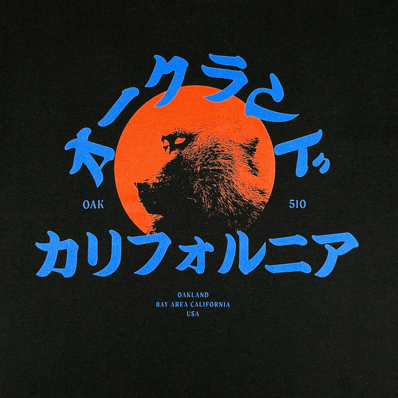Close-up of red snow monkey graphic and blue Asian written characters, Oak 510 wordmark & Oakland Bay Area California wordmark on black t-shirt.