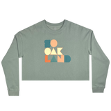 Cropped crewneck sage green sweatshirt with a full-color SOOAKLAND graphic wordmark on the front chest.
