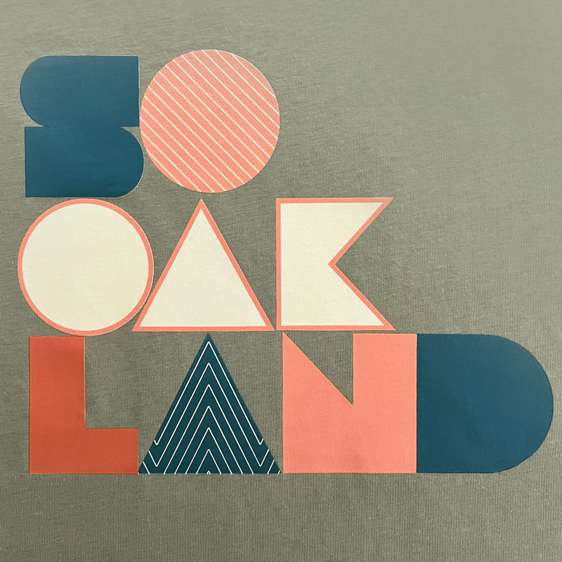 Close-up of SoOakland full-color wordmark on the front chest of a pistachio t-shirt.