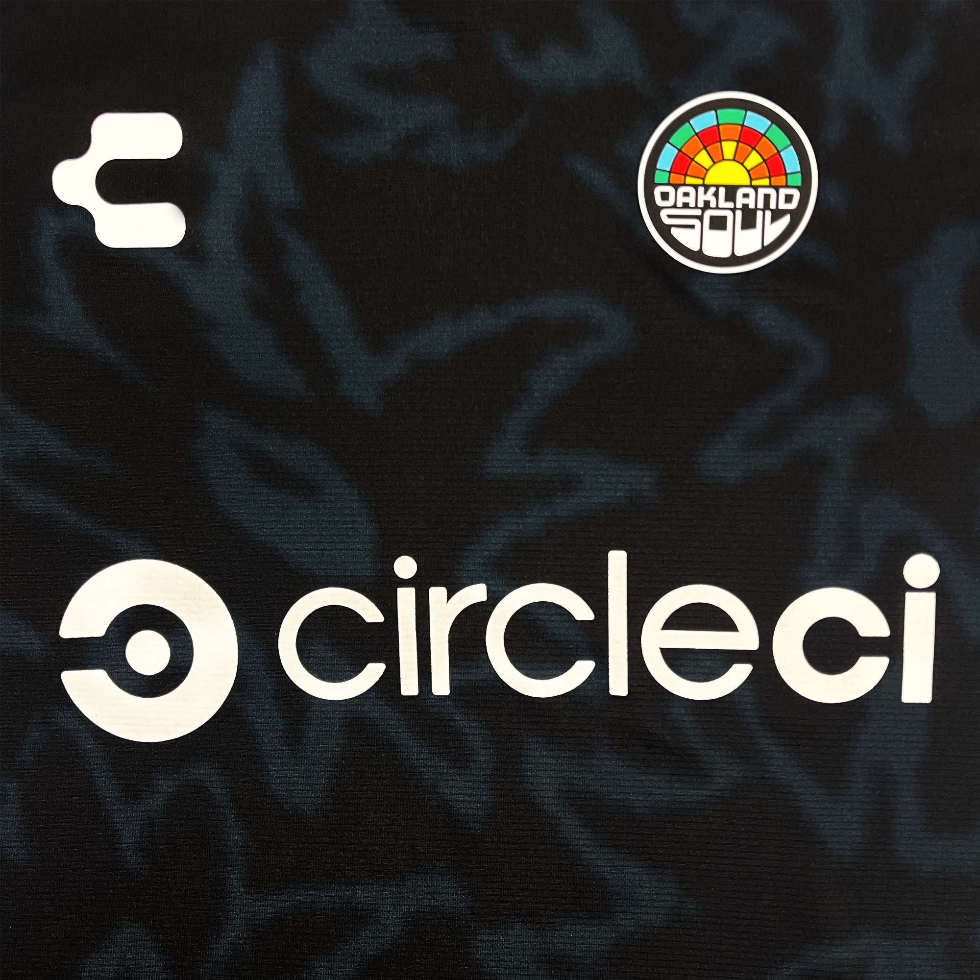 Detailed Front chest view of black color Oakland Soul x Charly soccer jersey with Oakland Soul crest on wearer's left chest , Charly logo on wearer's right chest and CircleCi logo centered in white.