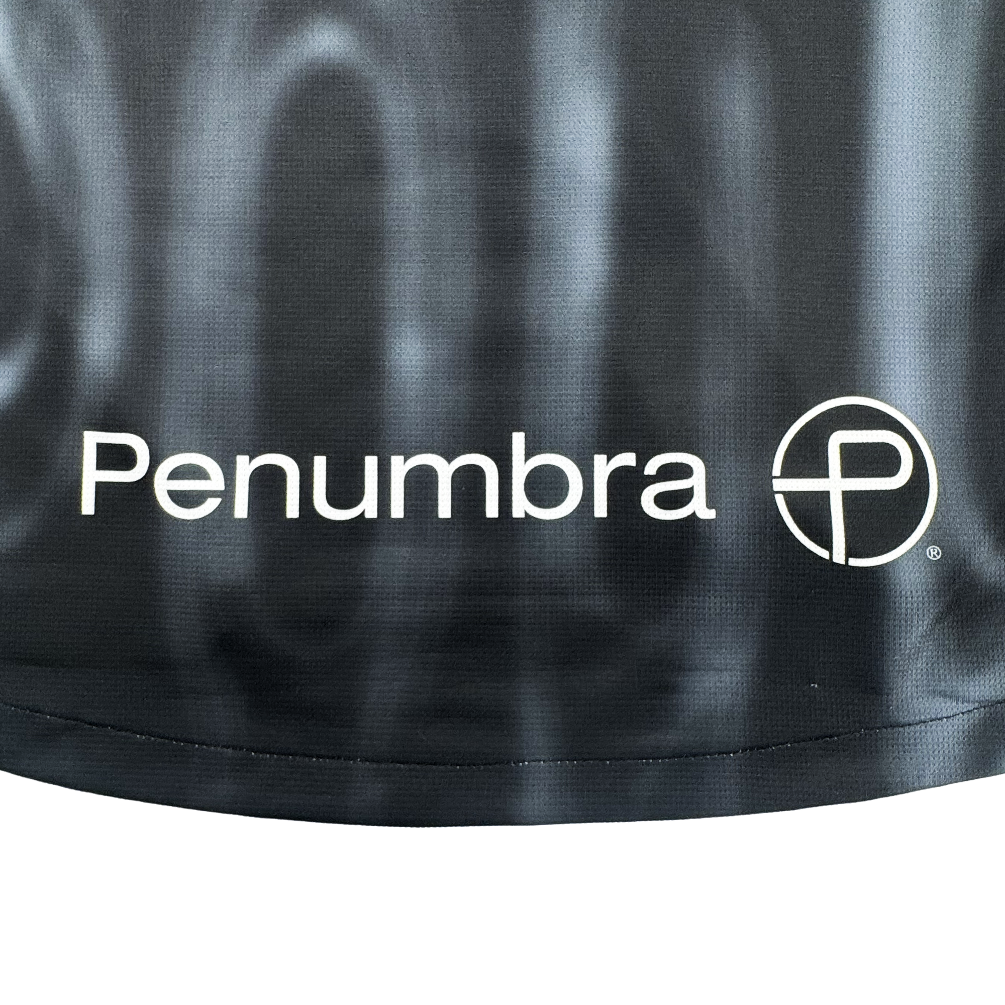 A close-up of the Custom 2026 OAKLAND SOUL SC SPIRIT JERSEY by Oakland Soul displays "Penumbra" in white beside a circular geometric logo with a stylized "P" on black Form Jersey fabric with a light gray wavy pattern in the background.