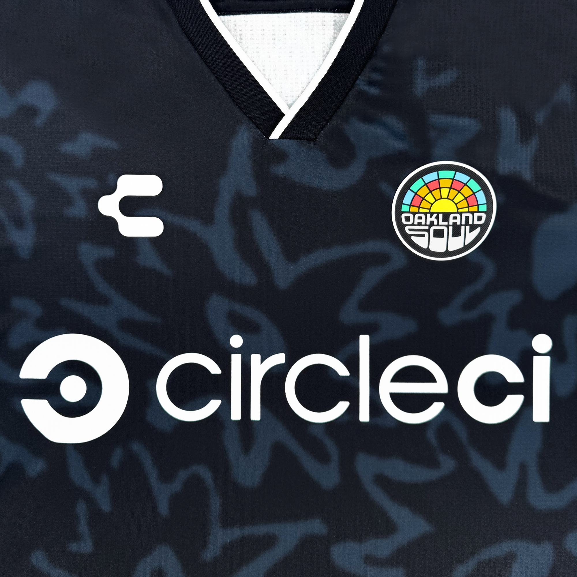 Close-up of the Custom Unisex Soul Bloom Kit by Oakland Soul, featuring abstract patterns, a white "circleci" logo, a small backward "C" brand mark, and the colorful Oakland Soul FC badge near the V-shaped collar.
