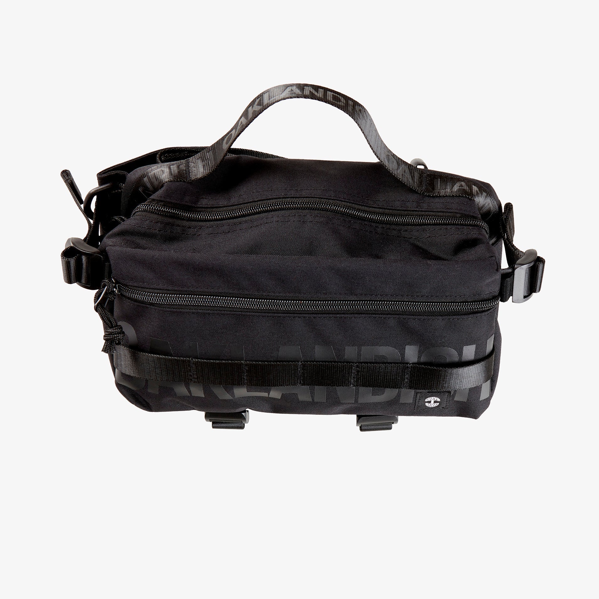 A black nylon hip bag with a black Oaklandish wordmark top zipper, front zipper, top handle, waist belt, & small white Oaklandish tree logo.