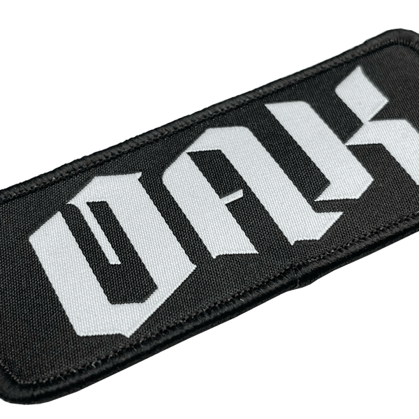 Close-up of woven black iron-on patch with white OAK wordmark in drip.