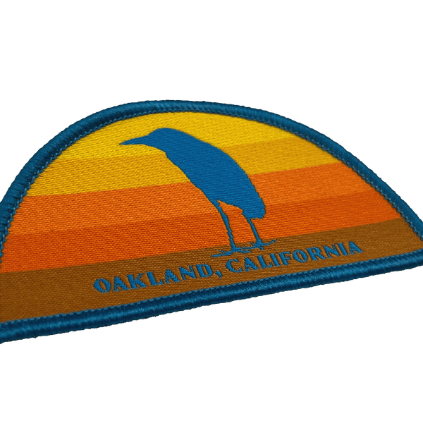 Close-up of multi-color iron-on half circle patch with night heron at sunset with Oakland, California wordmark.