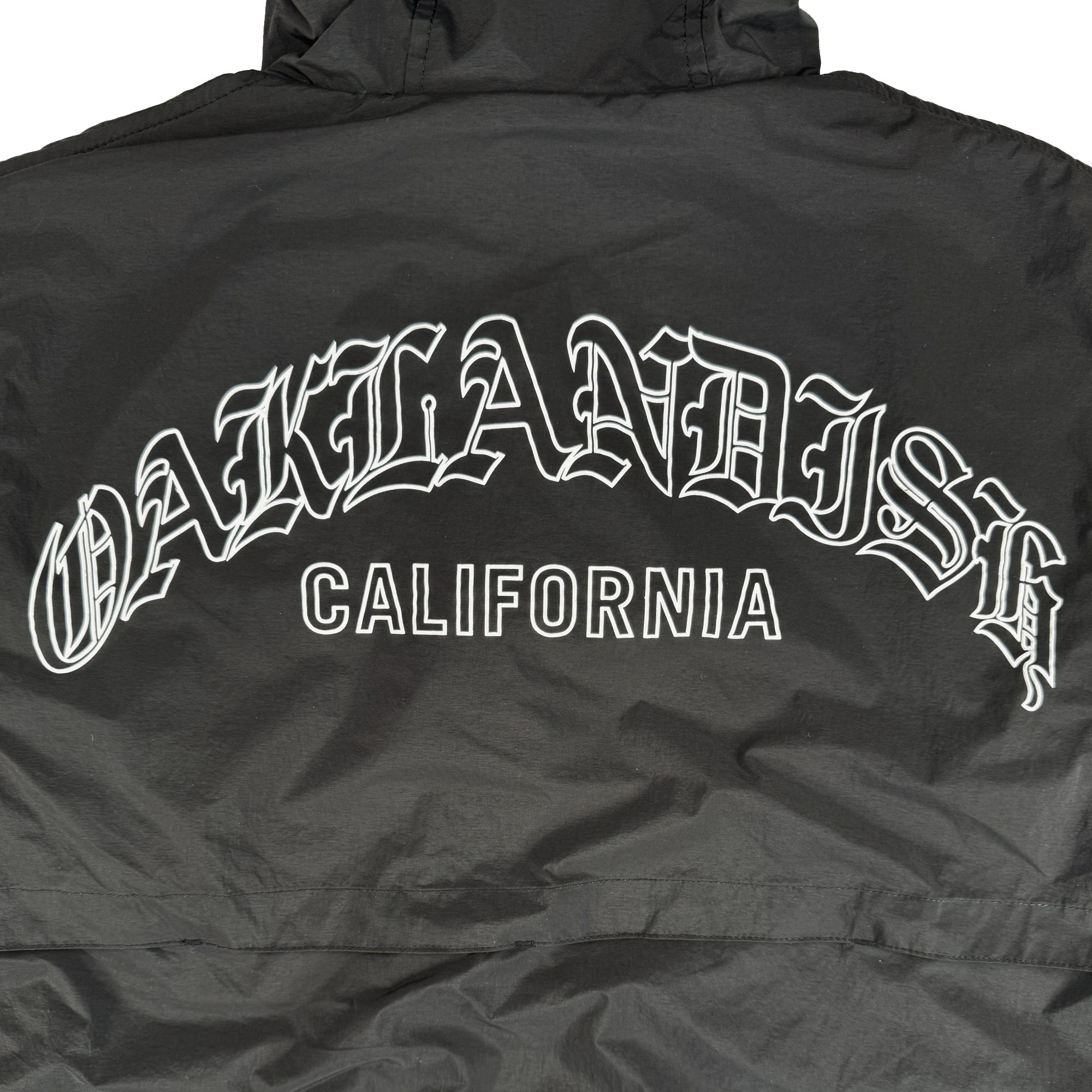 The Oaklandish Susurrus Track Top is a black men's zip jacket with bold white "OAKLANDISH" in gothic font above "CALIFORNIA" block letters on the upper back, shown laid flat to highlight the design.