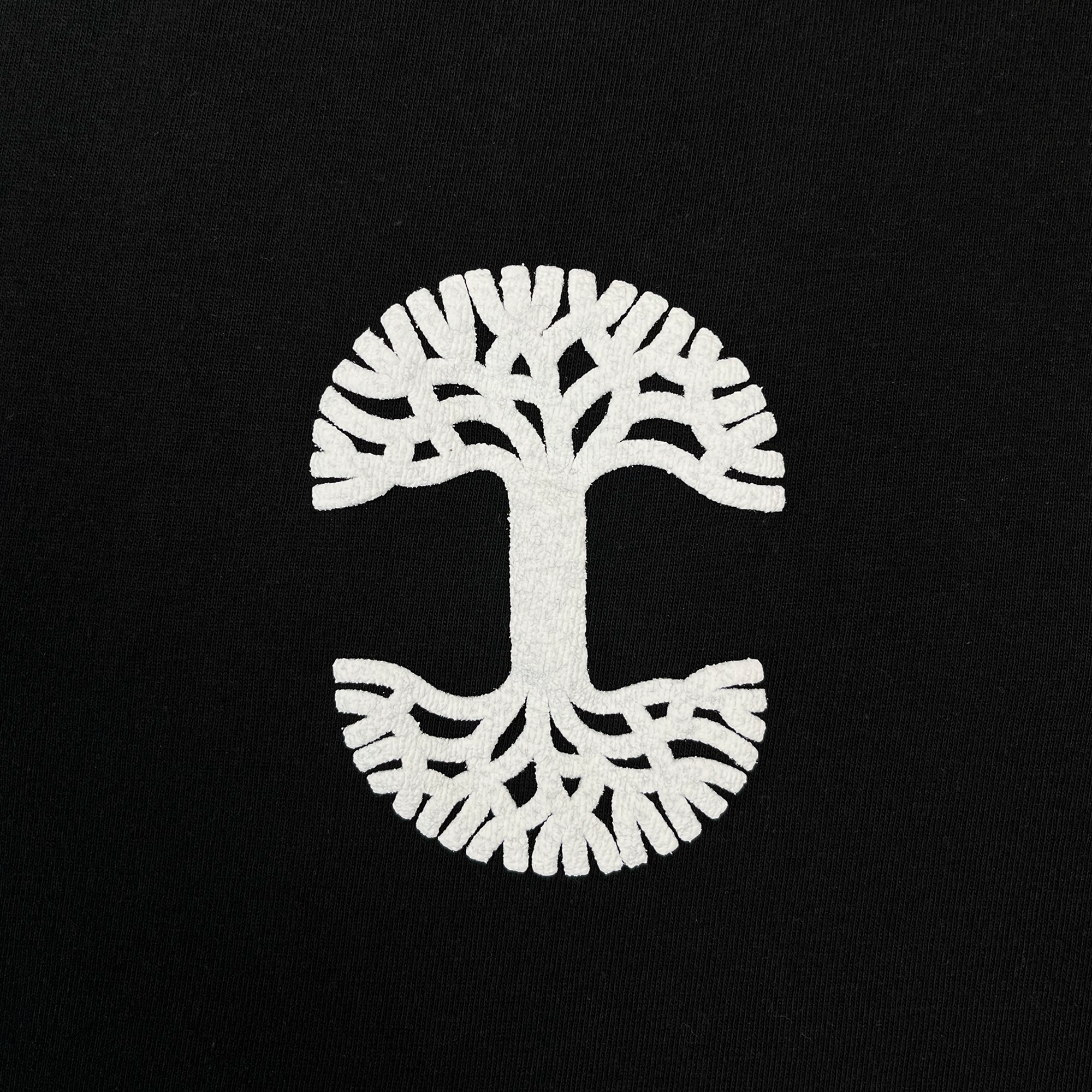 The Oaklandish Temple LS Tee features a striking white tree design with mirrored branches and roots, creating a symmetrical circular pattern reminiscent of both a tree and the letter “C” on a black background. Printed on 100% cotton, this men’s heavy-weight long sleeve t-shirt combines comfort with lasting durability.