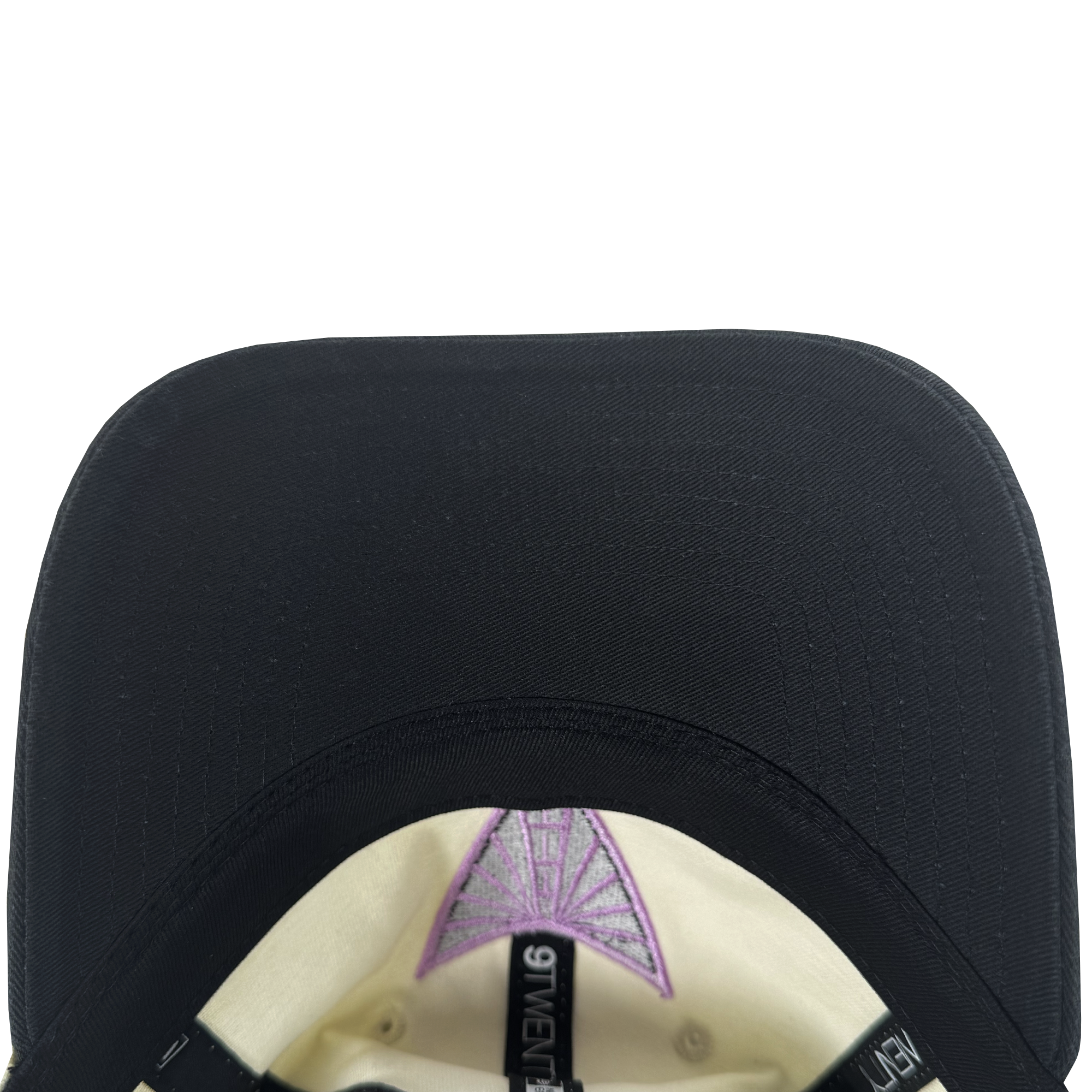 Close-up of the GSV WNBA 9FIFTY Snapback's brim underside. The cream lining has a purple triangle embroidery, plus black strips featuring "GIVENCHY" in white. A plain white background highlights the cap’s detailed design.
