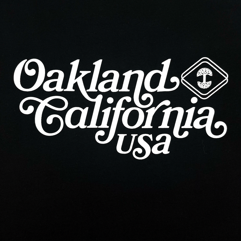 Close-up of Oakland, California, USA graphic in cursive and Oaklandish logo on a black t-shirt.