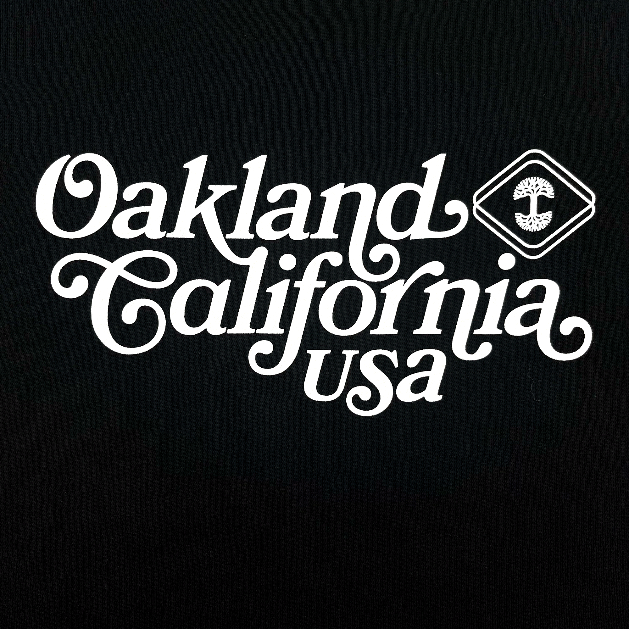 Close-up of Oakland, California, USA graphic in cursive and Oaklandish logo on an black women’s cut t-shirt.