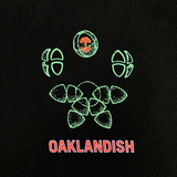Close-up of green and red Oaklandish worldwide graphic on the left chest wear side of a black t-shirt.