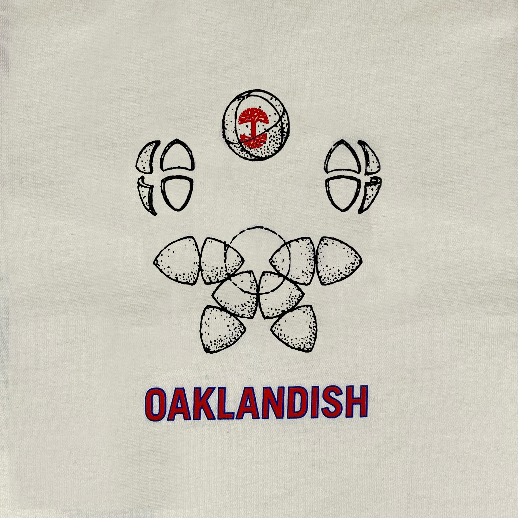 Close-up of Oaklandish worldwide graphic on the left chest wear side of a natural cotton-color t-shirt.