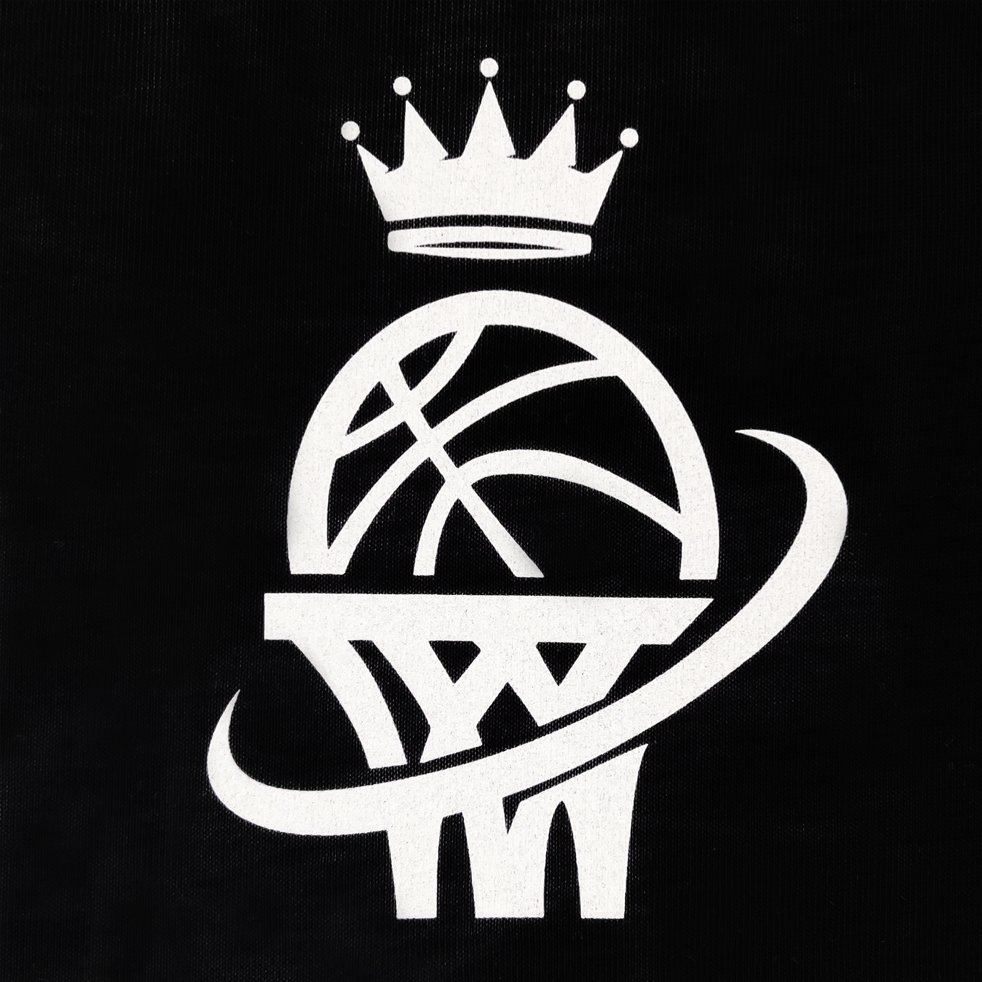 A black background features a white graphic of a basketball going through a hoop with a net. Above the basketball, a stylized crown with five points is placed, suggesting a royal or prestigious theme. A swoosh encircles the basketball, adding a dynamic element to this Oaklandish Legacy Tee celebrating women's sports.