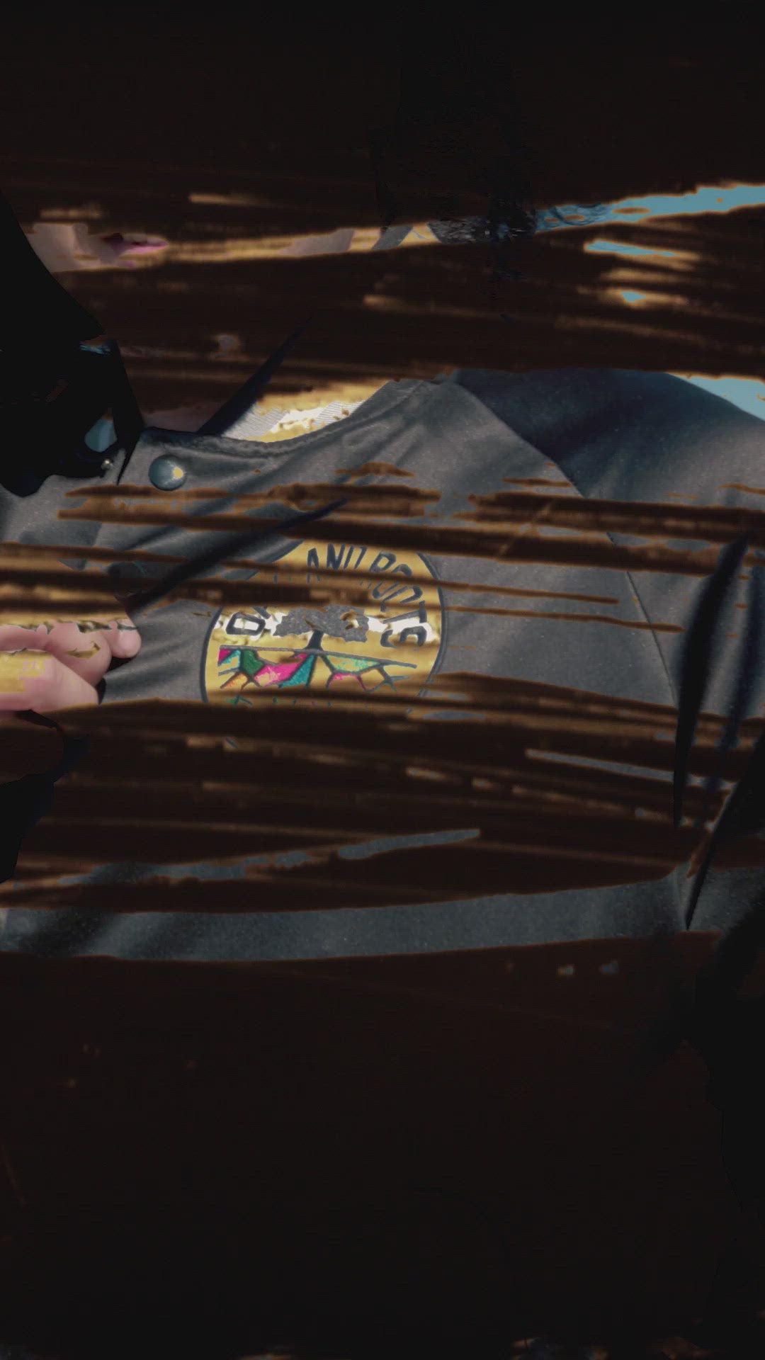 Two men outside in black satin jackets with striped collars & cuffs, buttons, and Roots SC logos and front pockets.