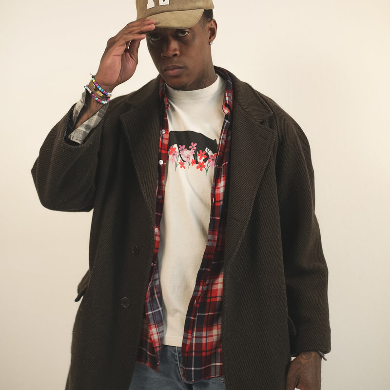Man wearing a creme t-shirt with bear and flower design created by artist Ant Bankxin with his hands holding the bill of his cap.