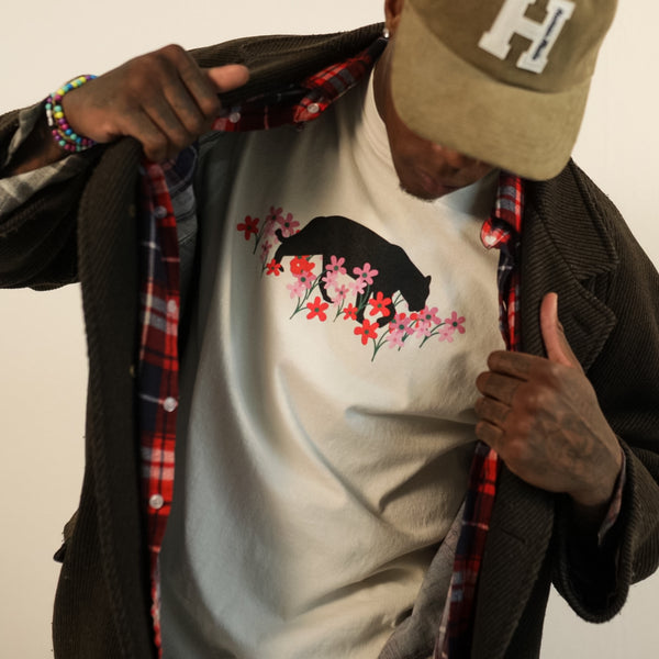 Man wearing a creme t-shirt with bear and flower design created by artist Ant Bankxin with his hands holding open his jacket.