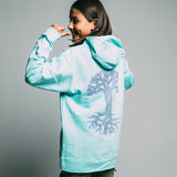 Girl standing back to camera showing off back side of a mint green youth hoodie with a large purple Oaklandish tree logo. 