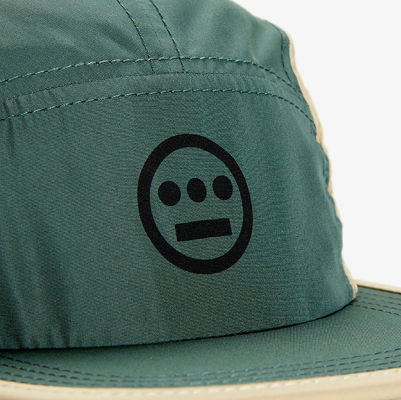 Detailed close-up of black Hieroglyphics hip hop logo on olive crown of a baseball cap.