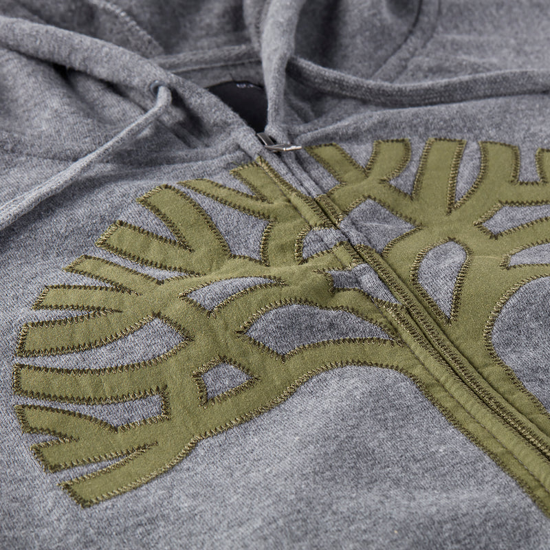 Close up of olive Oaklandish tree appliqué logo on the chest of a grey zip-up hoodie.