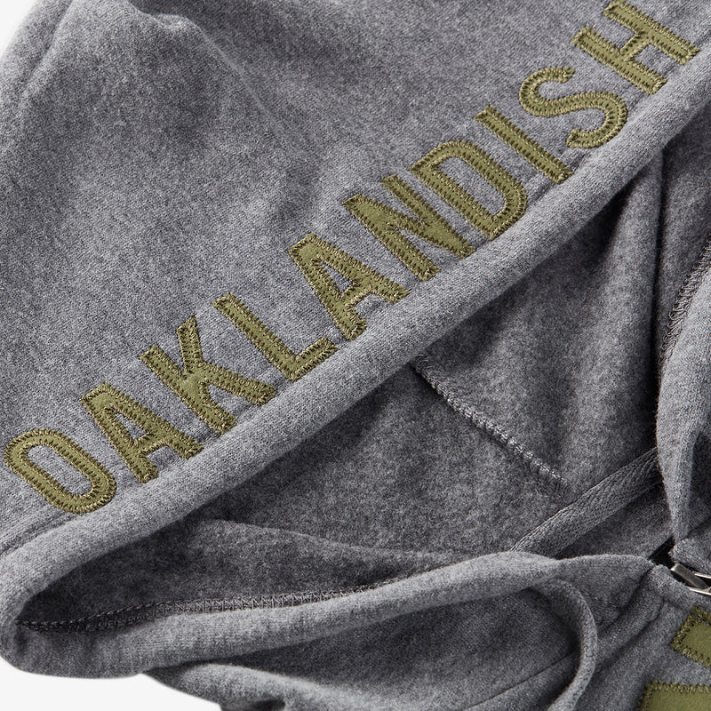 Close up of olive Oaklandish appliqué wordmark logo on the hood of a grey zip-up hoodie.