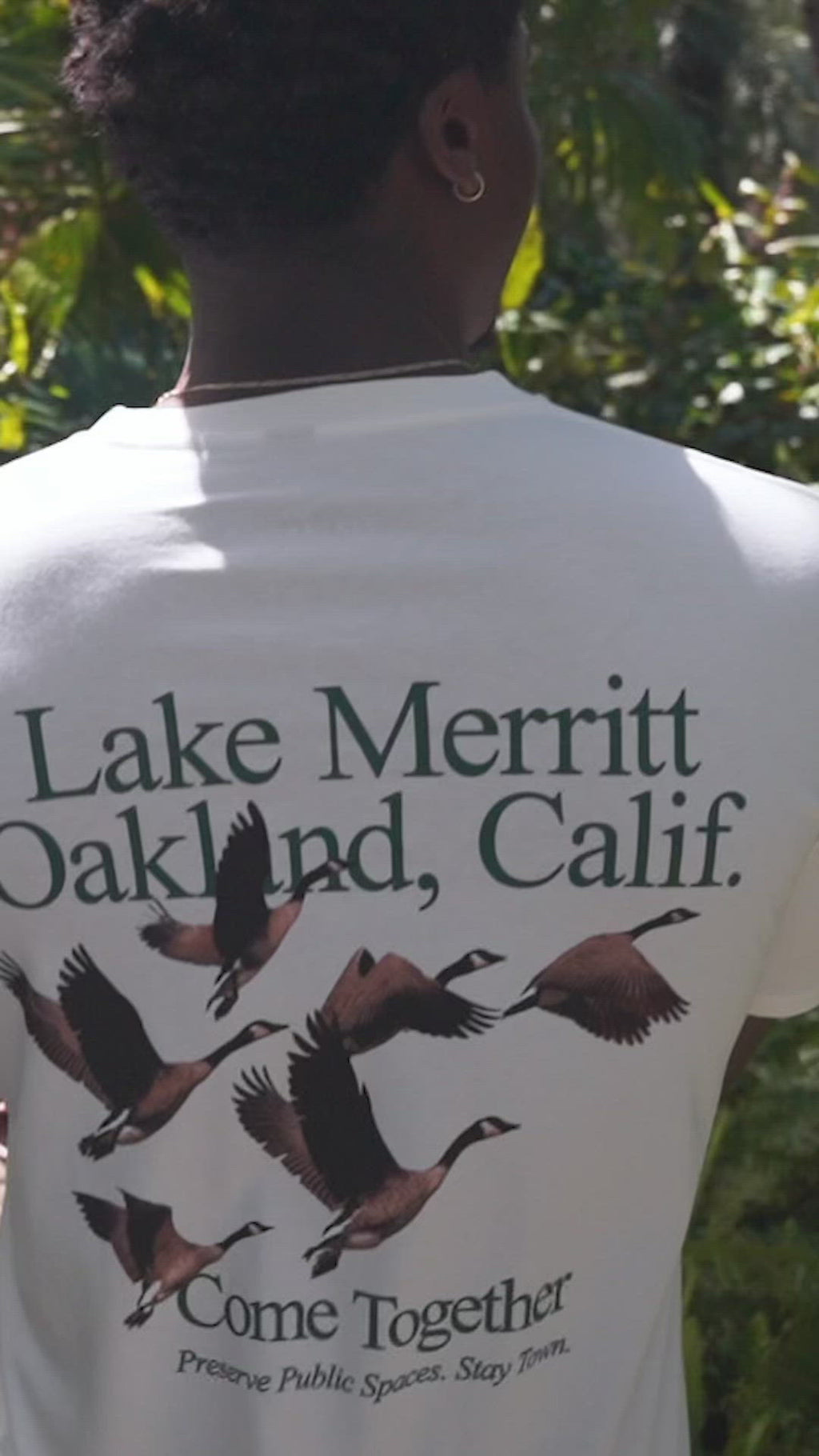 Man and woman walking in park wearing “Lake Merrit Oakland Calif. Come together” t-shirt.
