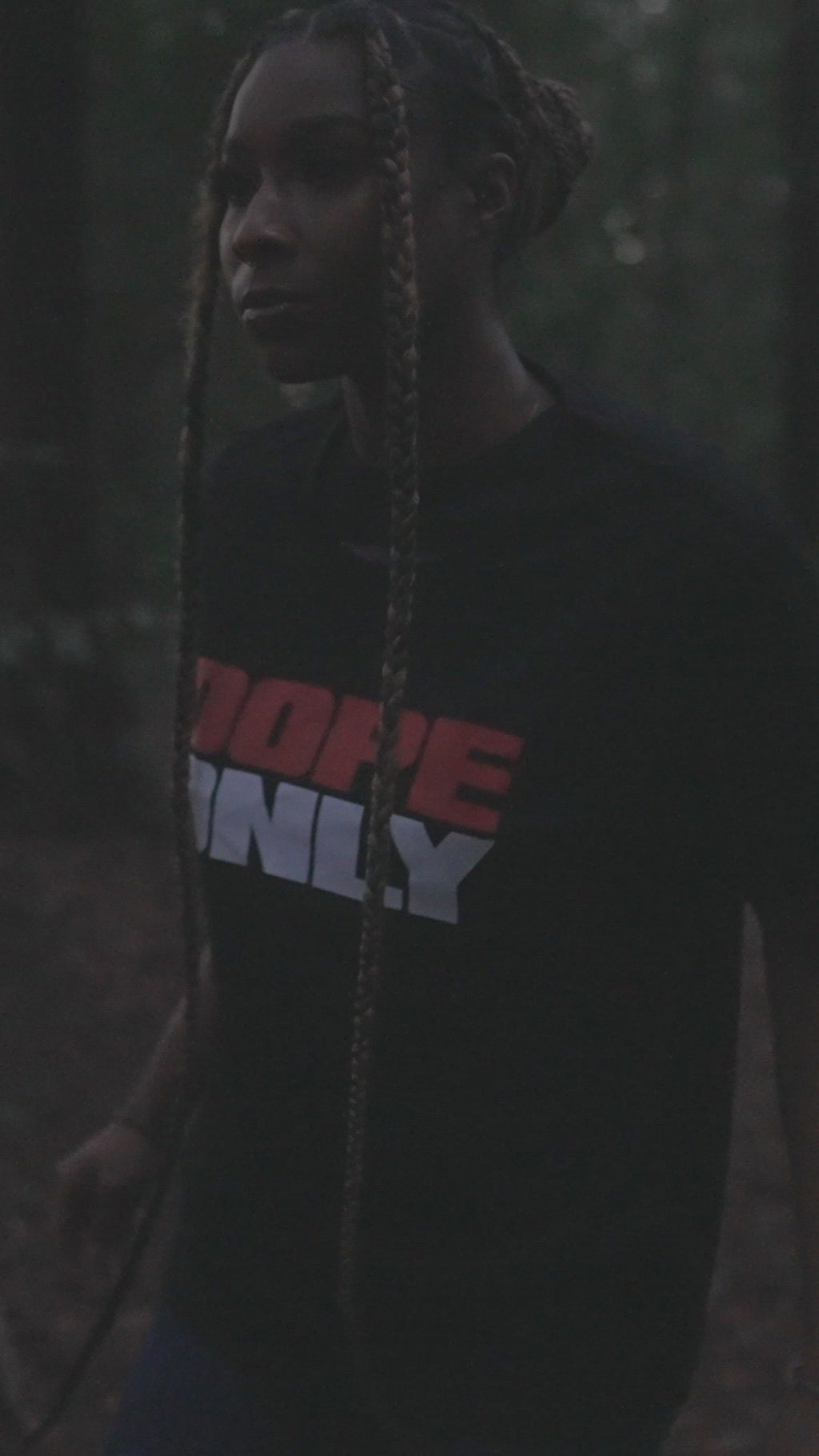 A woman walking in a forest wearing a black t-shirt with a large red and white DOPE ONLY wordmark logo on the chest.