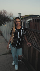 Woman standing outside in a white striped black baseball jersey with a black and white O for Oakland applique on the chest.