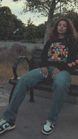 Woman and man sitting on a park bench in a long sleeve black t-shirt with flowers and birds designed by artist Jet Martinez. 