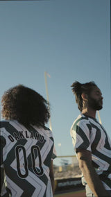 Man and woman outdoors in soccer jerseys with green and white zig-zag pattern and black Oakland O and Oaklandish tree logo.