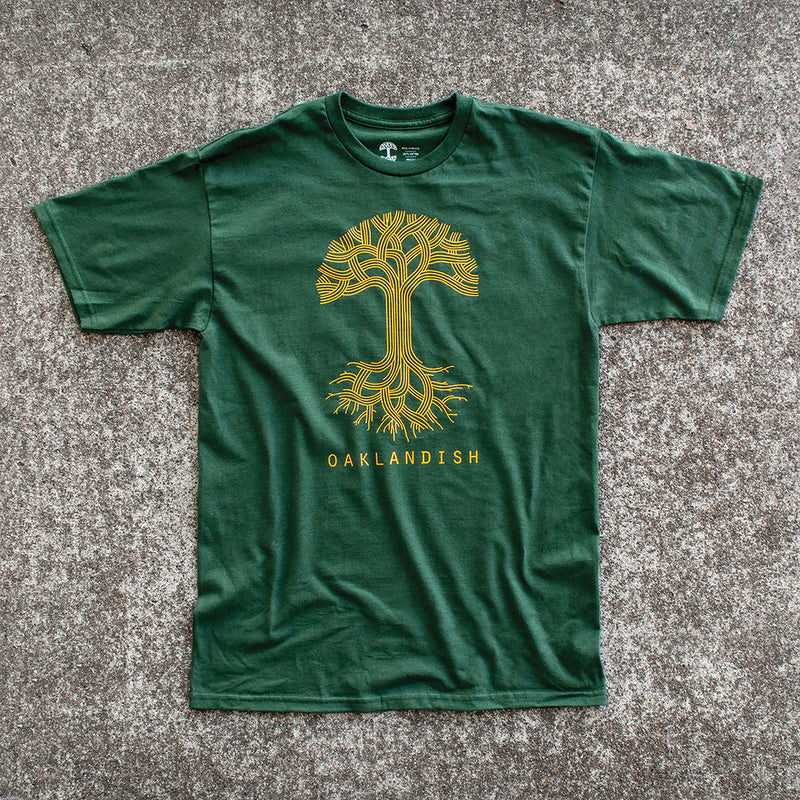A forest green t-shirt with a large white Oaklandish tree logo on the chest lying on cement.