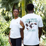Man and woman standing beside palms in “Lake Merrit Oakland Calif. Come together” t-shirts.