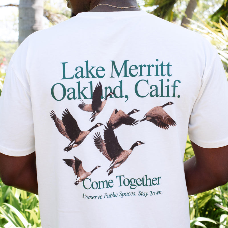 Back of natural cotton t-shirt on a man says “Lake Merrit Oakland Calif. Come together.” with flock of geese. 