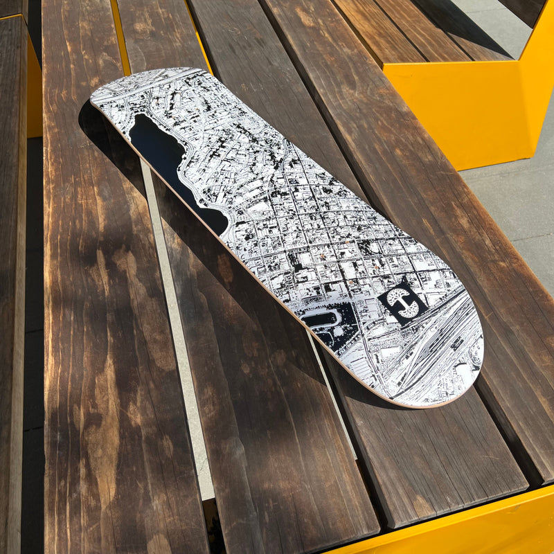 Skateboard deck with an aerial view photo of east of Lake Merritt and Oaklandish logo in black and white on outdoor picnic table.